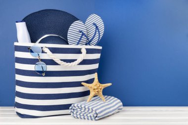 Mavi kumsal çantası ve ahşap masa üzerinde yaz aksesuarları.