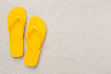 Kum arka planında parlak parmak arası terlikler, üst manzara. Yaz konsepti