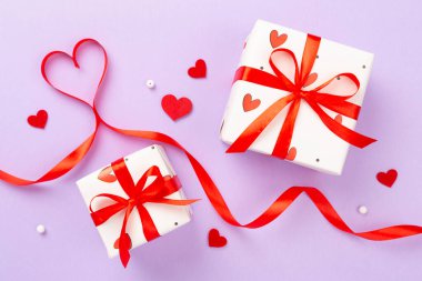 Renk arkaplanında kırmızı kalpler olan bayramlık hediye kutuları, üst görünüm
