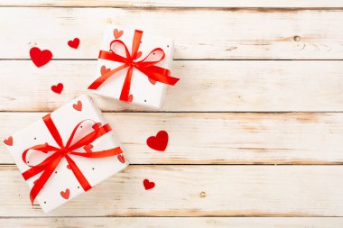 Ahşap zemin üzerinde kırmızı kalpler olan şenlikli hediye kutuları.