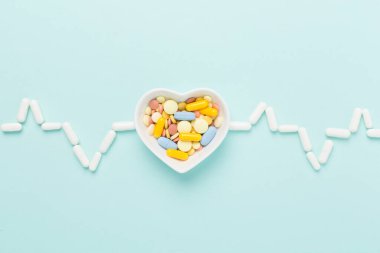 İlaçlar ve kalp şeklindeki çanak kardiyogramdan yapılmış. Renkli arka plan, üst görünüm.