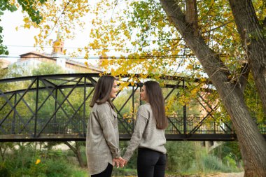 Aşık bir kadın, güzel bir sonbahar gününde parkta gülümseyerek ve el ele tutuşarak yüz yüze durur..