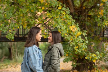 Gülümseyen lezbiyen çift bir sonbahar günü parkta durup birbirlerine bakıyorlar.. 