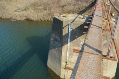 Water meter bar under rusted old bridge on shallow river