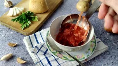 The chef pours borscht into an empty white plate.  Ukrainian traditional soup.  Borscht