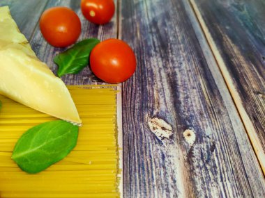 Çiğ spagetti, kiraz domatesleri, ıspanak yaprakları ve ahşap bir masada parmesan peyniri. Kapat. 