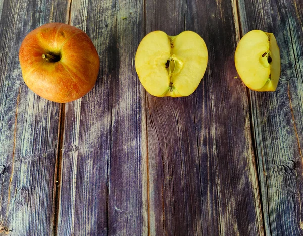 Whole red apple, half and quarter on a wooden table. View from above