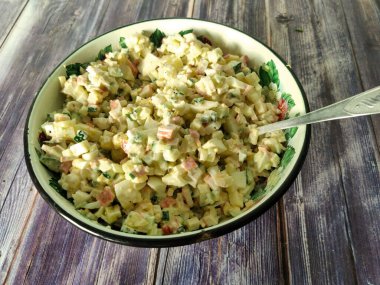 New Year's salad of crab sticks, cucumbers, boiled potatoes, chicken eggs, corn and mayonnaise. Salad in a metal bowl with a spoon. View from above