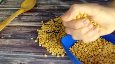 Split peas.  A man with his hand collects halves of peas from a wooden table into a blue bowl.  Shooting from above
