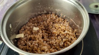 Adding butter to boiled buckwheat in a saucepan.  Close-up