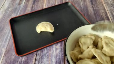 Haşlanmış hamur köftelerini saygılı bir şekilde metal bir kaseden siyah bir tabağa koymak.