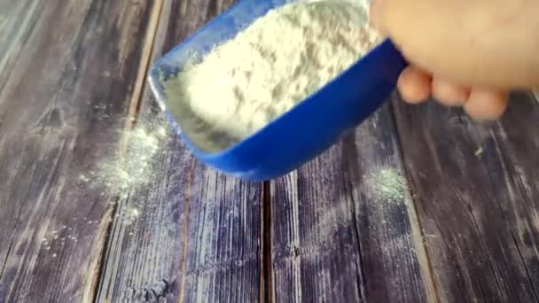 小麦粉は青いプラスチック製の皿から木製のテーブルの上に注ぐ 上からの撮影 — ストック動画