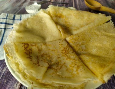 Fried pancakes on a white plate on a wooden table, sour cream in a gravy boat. Close up 