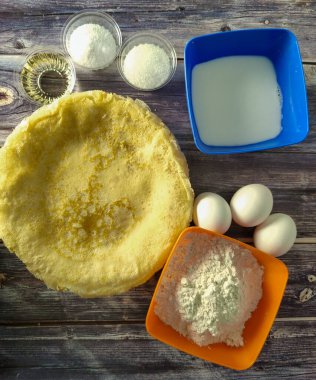 Fried pancakes, wheat flour, milk, chicken eggs, vegetable oil, salt and sugar on a wooden table.  Ingredients for fried pancakes