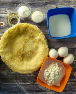 Fried pancakes, wheat flour, milk, chicken eggs, vegetable oil, salt and sugar on a wooden table.  Ingredients for fried pancakes