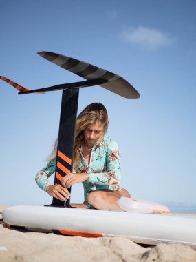 Kafkasyalı sarışın genç kadın kumsala hidrofolyo sörf tahtası kuruyor.