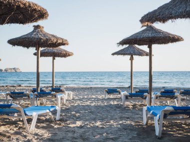 Kumsalda mavi güneşli yataklar, hasır şemsiyeler ve arka planda deniz. Paguera, Calvia 'daki Akdeniz sahili Gran Tora