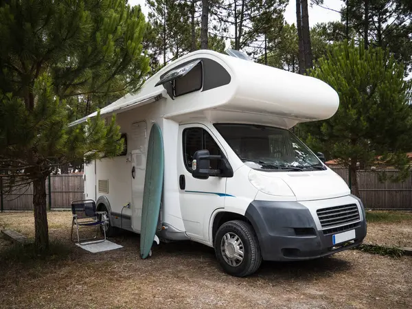 Kamp yerine park etmiş bir karavan, bir sandalye ve dışarıda sörf tahtası.