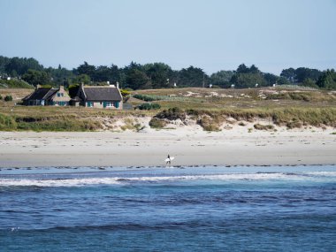 A surfer is walking by Pors Carn beach in French Brittany clipart