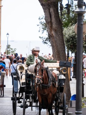 Palma de Mallorca, İspanya; 17 Eylül 2024: Turistlerle dolu eski Palma de Mallorca kasabasında müşterileri bekleyen bir at arabası sürücüsü