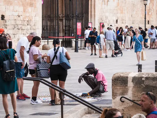 Palma de Mallorca, İspanya; 17 Eylül 2024: Katedral yakınlarındaki Eski Palma de Mallorca kasabasında turistlere mal satan bir sokak satıcısı, çeşitli ziyaretçi kalabalığı tarafından çevrelenmiş durumda..