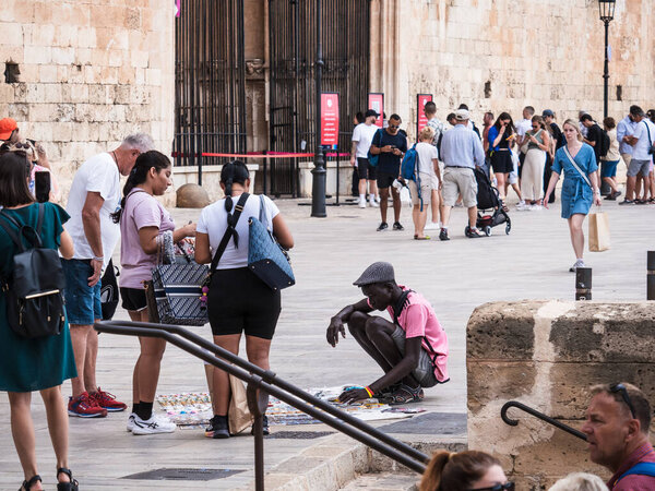 Пальма-де-Майорка, Испания; 17 сентября 2024: Уличный торговец, продающий товары туристам в Старом городе Пальма-де-Майорка рядом с кафедральным собором в окружении разнообразной толпы посетителей.