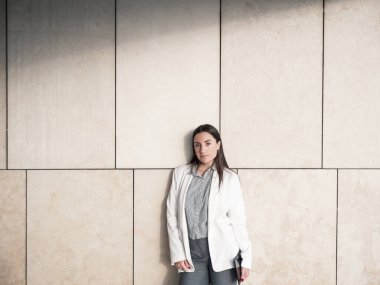 Kendine güvenen, resmi giyinmiş iş kadını modern bir duvara yaslanıyor.