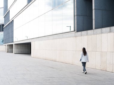 Bir iş kadını şehirdeki modern bir mimari binanın önünden geçiyor..