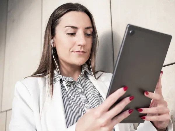 Modern ofis ortamında kulaklıklı dijital tablet kullanan bir iş kadını.