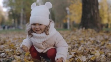 Sonbahar parkında yaprakları olan küçük bir kız. Yavaş çekim
