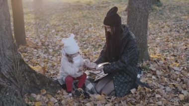Anne ve küçük çocuk bir sonbahar parkında ellerinde bir kitapla, mutlu bir aile, anneyle yaşamak, doğa yürüyüşü.