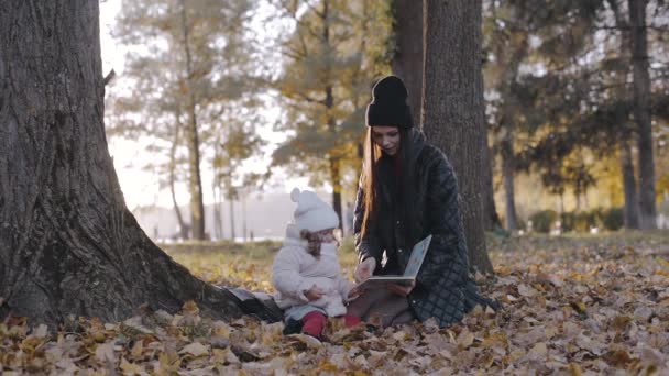 妈妈和小孩在秋天的公园里 手里拿着一本书 快乐的家庭 和妈妈一起生活 自然漫步 — 图库视频影像