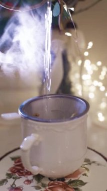 Bir bardağa yakın çekim su dök. Arka planda süslenmiş noel ağacı. Kış tatili konsepti. Evde yeni yılı kutluyoruz. Ağır çekim. Dikey video