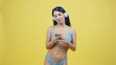 Beautiful young woman in headphones on a yellow background listening to music and dancing. Posing in the studio