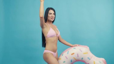 Beautiful woman smiling holding rubber ring, dancing and enjoying their summer vacation on blue background isolated. Happy trip concept