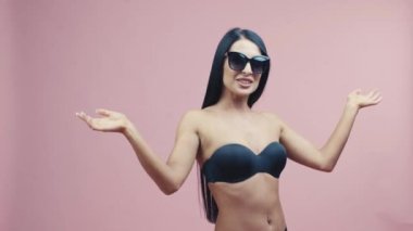 beautiful woman in swimsuit and sunglasses standing on a pink background, positive emotions. Summer vocation happy trip concept