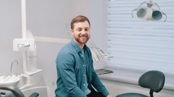 歯科医院で幸せな患者 成功した歯科治療後の魅力的な笑顔と健康的な歯を示す肖像ハンサムな若い男 — ストック動画