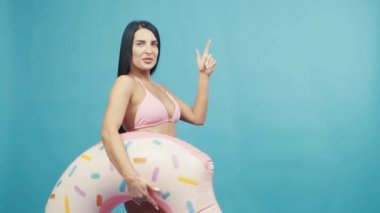 Beautiful woman smiling holding rubber ring and enjoying their summer vacation on blue background isolated. Happy trip concept
