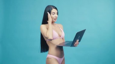 Beautiful woman in a pink swimsuit with laptop enjoying their summer vacation on blue background. Happy trip concept