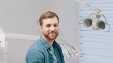 Happy patient in dental clinic. Portrait handsome young man showing charming smile and healthy teeth after successful dental treatment