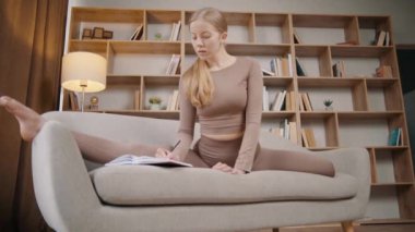 Genç kız kitaplarla dolu bir odada yoga yapıyor, kız elinde defterle esniyor.