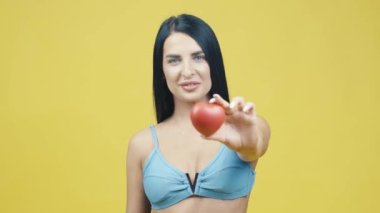 Sarı arka planda elinde kırmızı bir kalple kameraya poz veren güzel bir genç kadın.