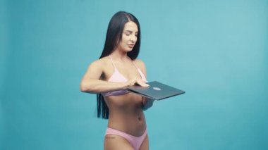 Dizüstü bilgisayarla gülümseyen güzel bir kadın mavi arka planda yaz tatilinin tadını çıkarıyor.