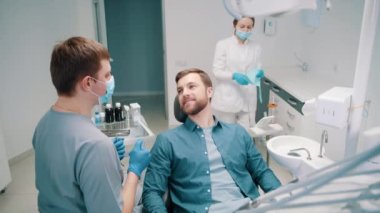 Erkek bir doktor bir hastayla diş tedavisi planını tartışıyor. Diş hekimliği. Diş sağlığı kliniği. Arka planda, bir kadın doktor bir hastayı hazırlıyor.