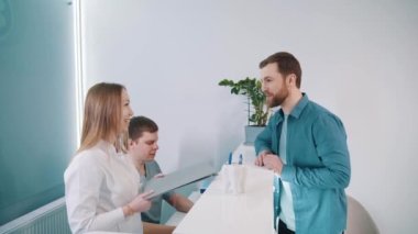 Geniş bir modern klinikte, genç bir hasta resepsiyondaki doktorlarla iletişim kurar, sonuçları kontrol eder ve doktor kontrolüne gider.