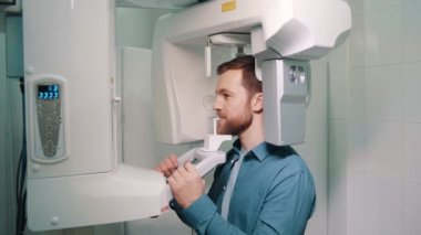 Genç bir erkek hasta ortopedi makinesi kullanılarak ağız boşluğunda panoramik röntgen çekiliyor. Modern diş kliniğinde tomografi tarayıcısı