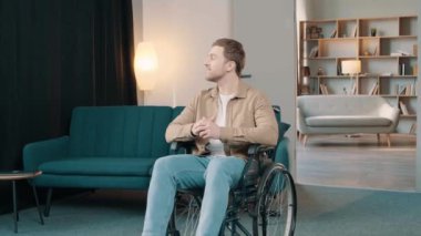 Odasında tekerlekli sandalyede oturan genç beyaz adam mutlu ve mutlu görünüyor.