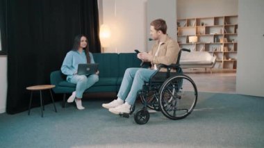 Çekici, gülümseyen, tekerlekli sandalyede sakat bir adam. Evde güzel karısı ve laptopuyla birlikte telefon ediyor.