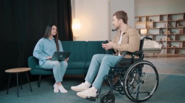 Çekici, gülümseyen, tekerlekli sandalyede sakat bir adam. Evde güzel karısı ve laptopuyla birlikte telefon ediyor.