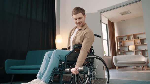Jovem Atraente Sorridente Homem Cadeira Rodas Levantando Halteres Quarto Ensolarado — Vídeo de Stock